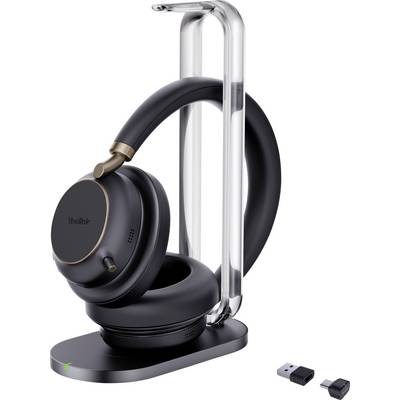 Egy fekete, aranyozott részletekkel díszített fejhallgató egy elegáns állványon pihen. Mellette egy kis USB-adapter kerül bemutatásra, amely a vezeték nélküli kapcsolatra utal.