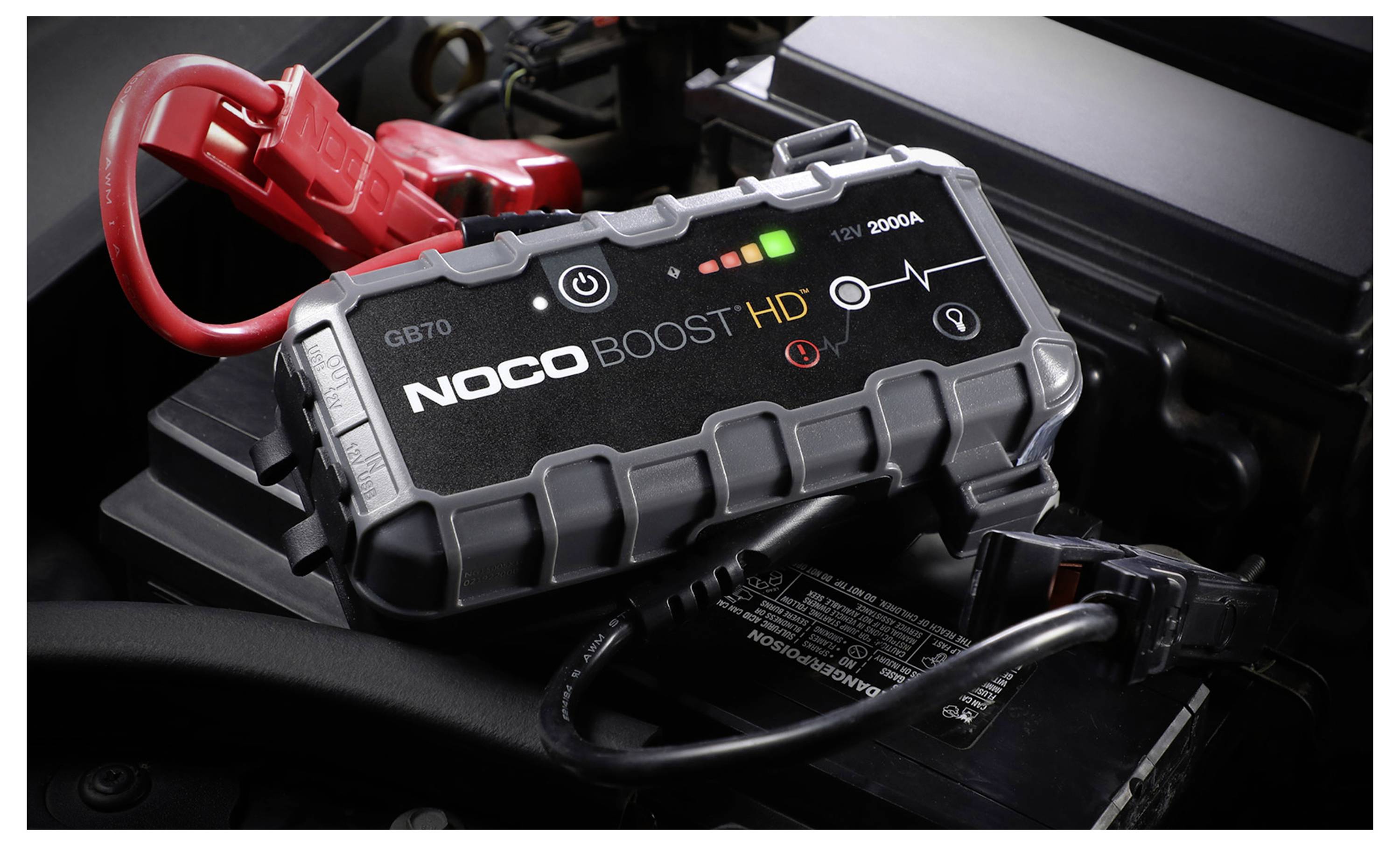 NOCO Boost HD hordozható autóakkumulátor indítósegéd piros és fekete karokkal, amely egy járműakkumulátorhoz csatlakoztatva van.