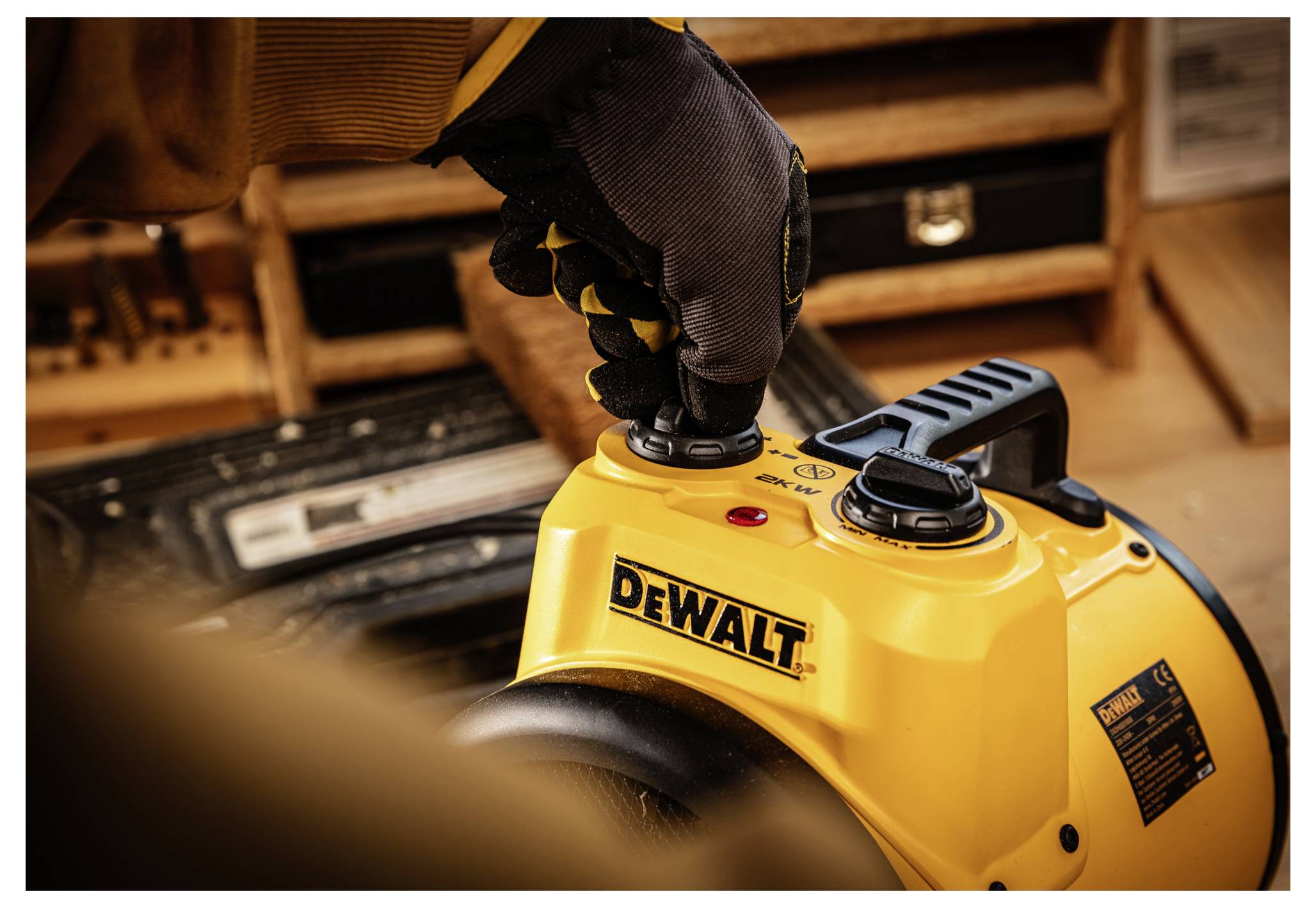 Kesztyűs kéz megnyomja a vezérlőgombot egy sárga DEWALT elektromos szerszámon a műhelyben.