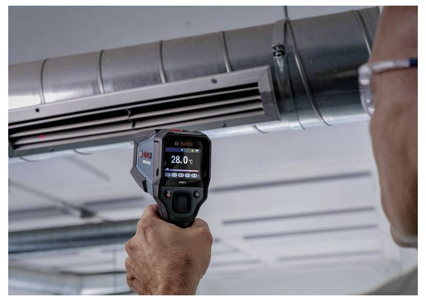 A személy termokamerát használ a mennyezeti HVAC csatornázat hőmérsékletének mérésére, az eszköz 28,0°C-ot mutat.