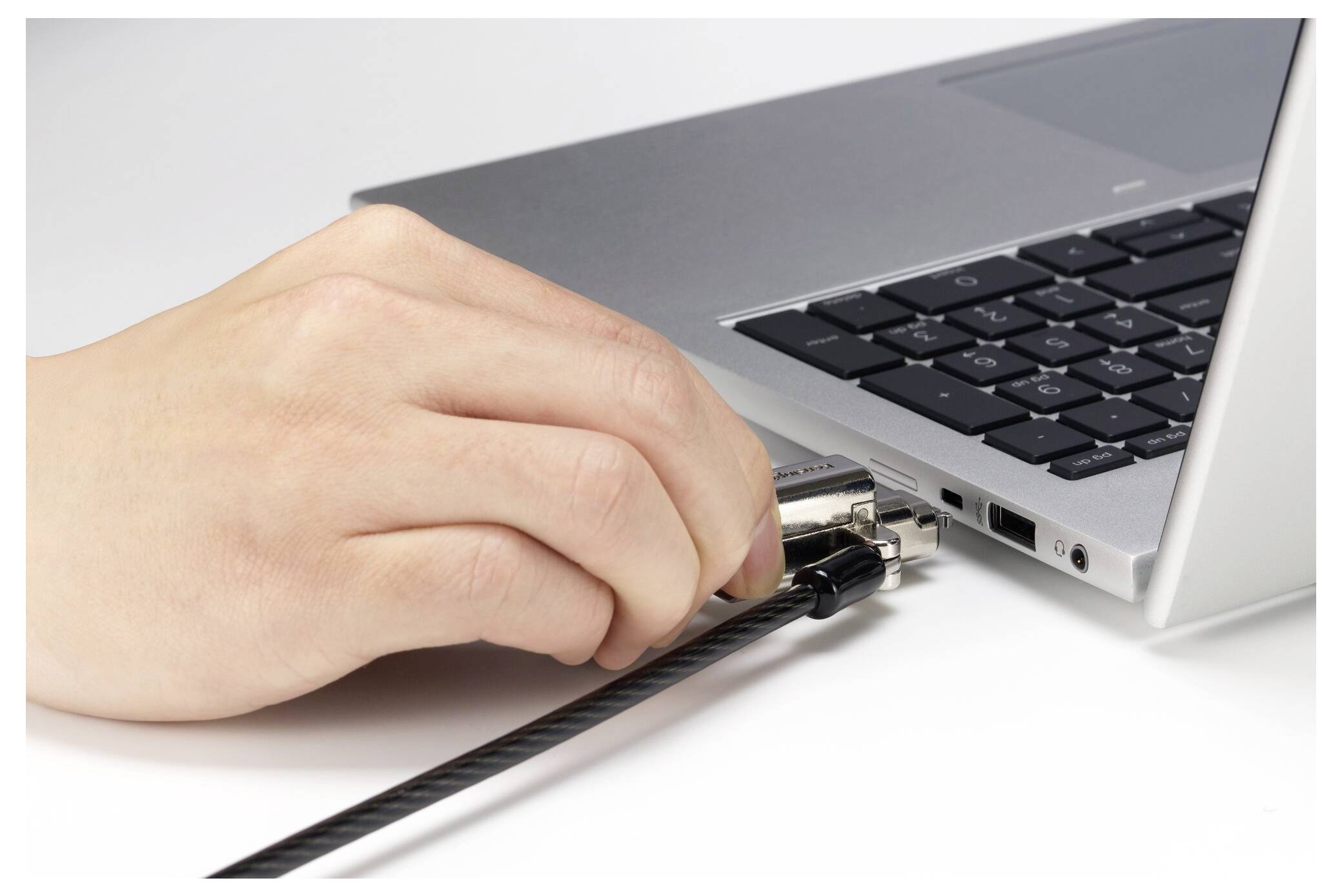 Kéz egy kábelt bedugva a laptop oldalsó portjába fehér felületen.