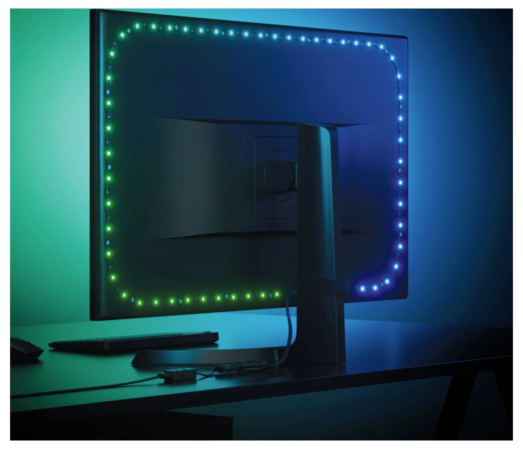 Egy asztali monitor hátoldalának nézete egy asztalon, zöld és kék LED-fényekkel körvonalazva egy sötét szobában.