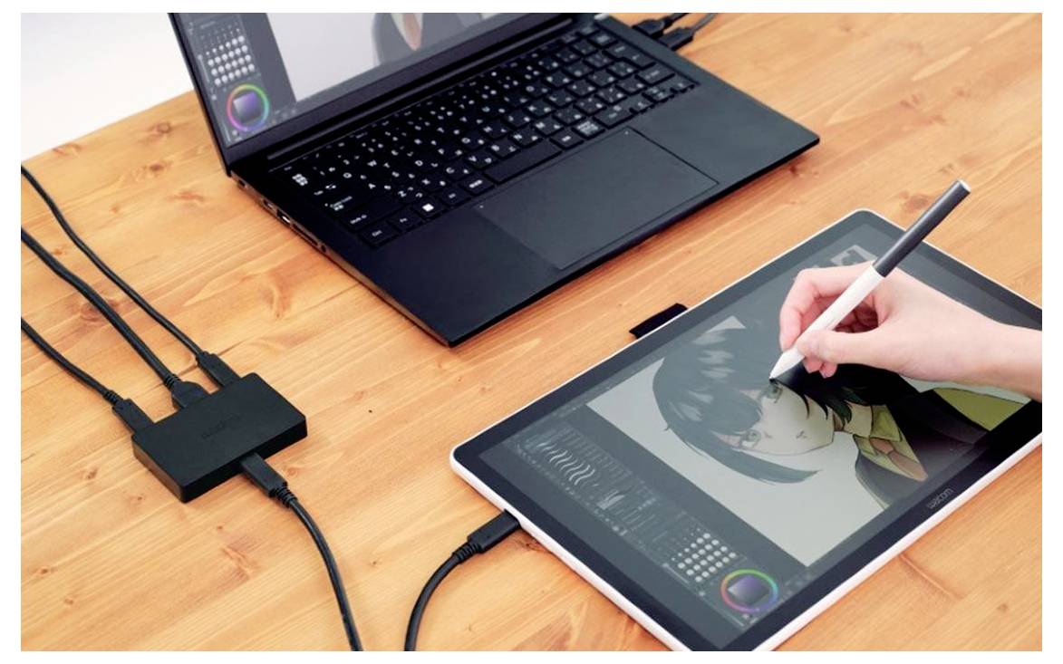 Kéz toll segítségével egy grafikus tablón dolgozik egy laptop mellett, amely digitális illusztrációra vagy fotószerkesztésre utal, egy faburkolatú íróasztalon.