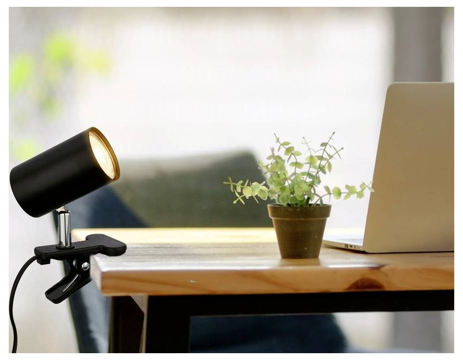 Asztal egy fekete csippanható lámpával, egy kis cserepes növénnyel és egy nyitott laptoppal egy világos ablak közelében.