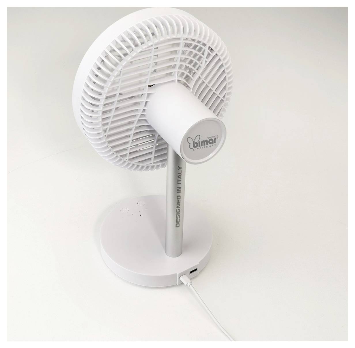 Fehér asztalfeltéti elektromos ventilátor kerek talppal, dönthető fejrésszel és látható tápkábellel síma háttéren.
