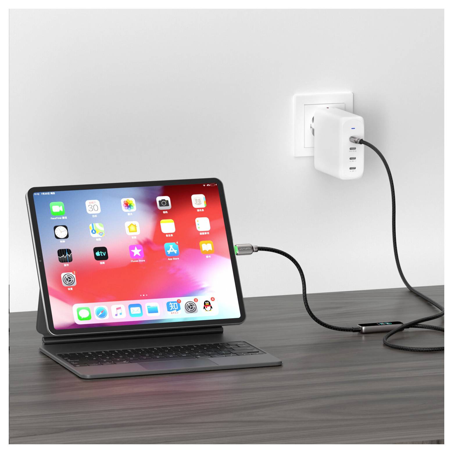 iPad egy billentyűzetállványon egy asztalon, amely faliósztóról vezetéken és tápegységen keresztül töltődik.
