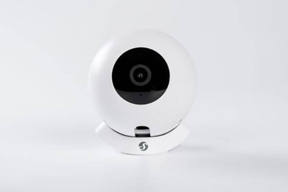Fehér biztonsági kamera egy állványon, elöl néző pozícióban, fekete kör alakú lencsével a közepén, egyszerű fehér háttéren.