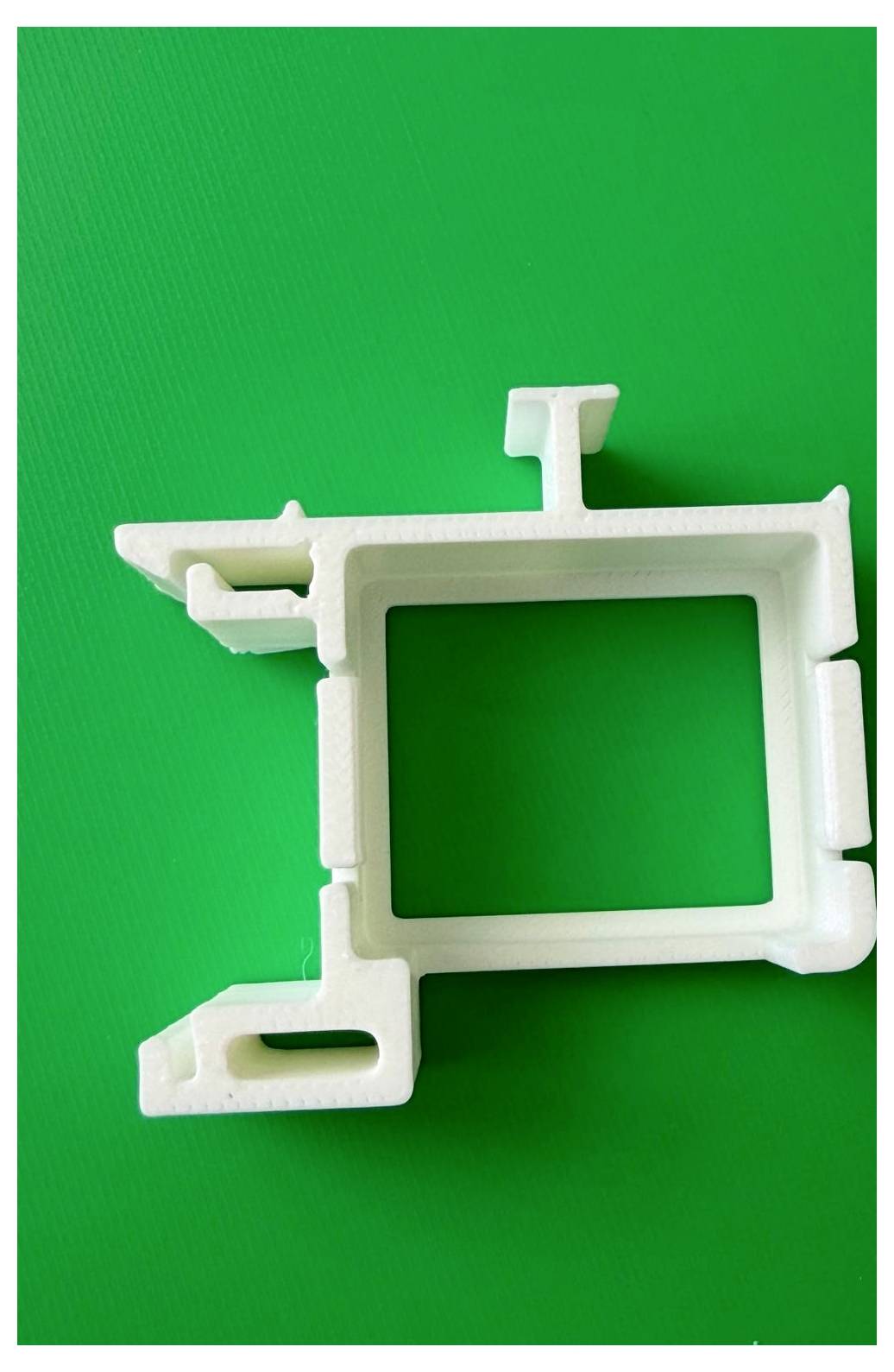Fehér műanyag szerelési klip vagy tartókonzol világoszöld háttéren, átlós nézetben mutatva.