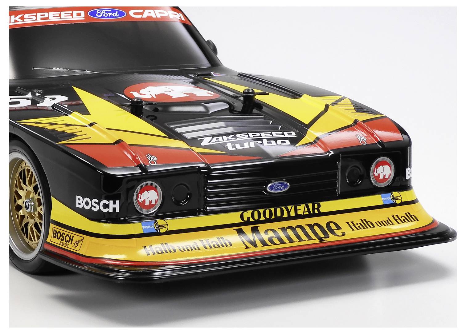 Fekete, sárga és piros Ford Capri versenyautó elölnézete szponzori matricákkal egy stúdió fehér háttéren.