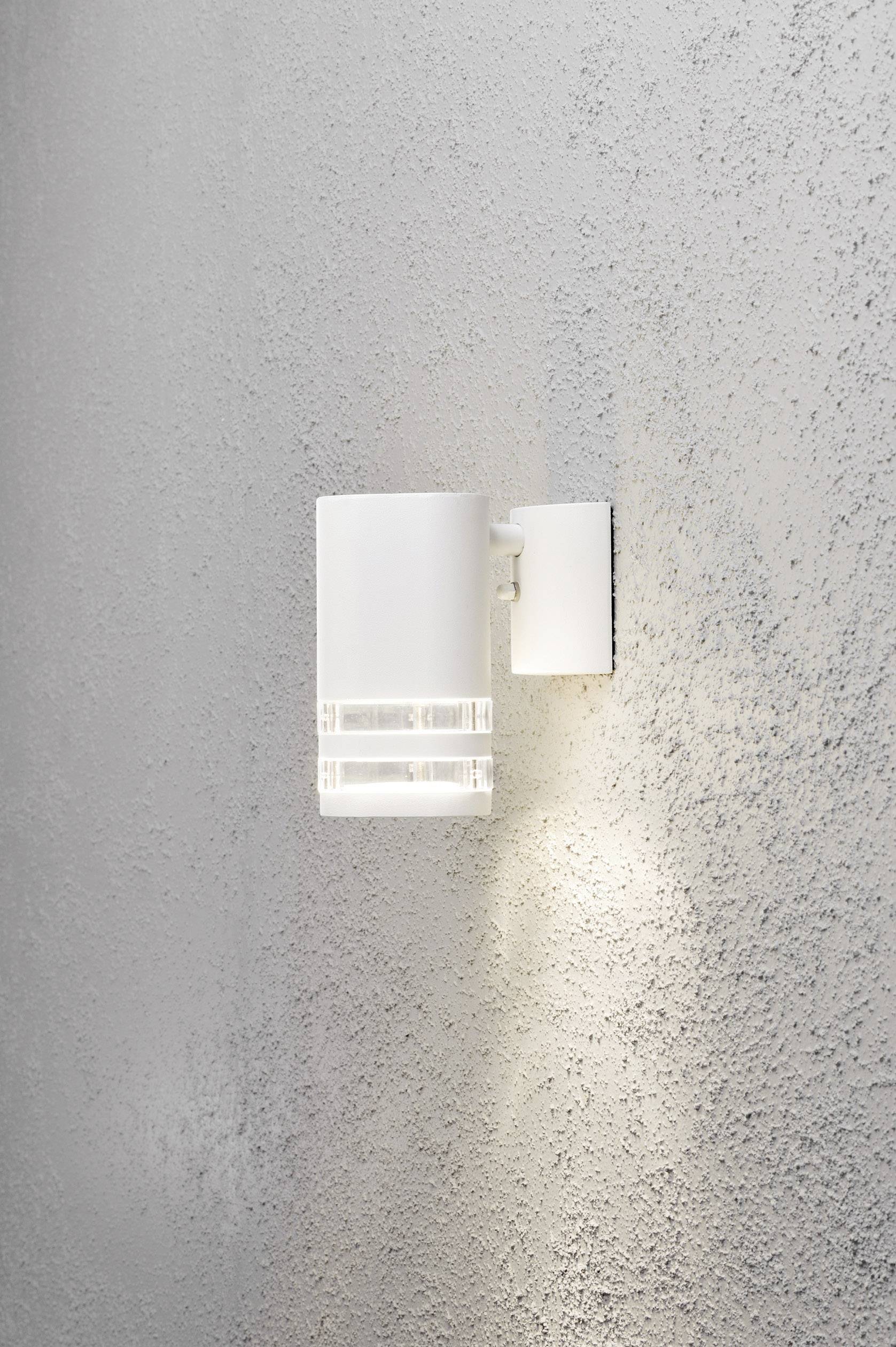 Fehér fali lámpa szürke fal előtt, amely meleg fényt sugároz. Modern design egyenes vonalakkal. Tökéletes hangulatvilágításhoz.