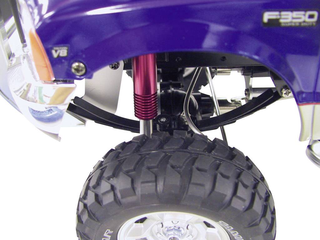 Egy terepjáró nagy, robusztus kerekének közeli felvétele, piros lengéscsillapítóval és a járómű kék részleteivel a háttérben.