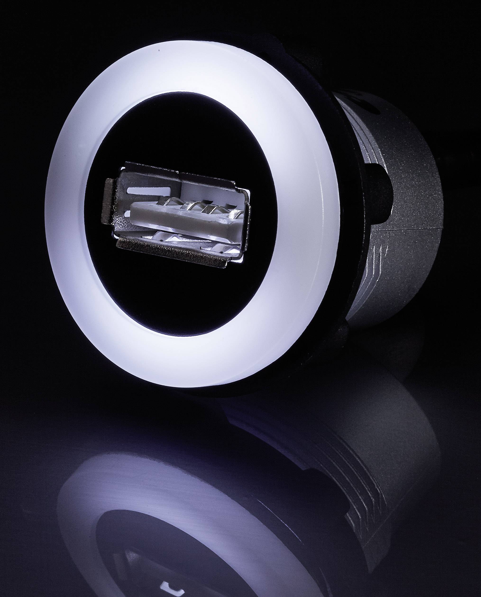 USB-csatlakozó világító gyűrűvel, sötét háttér előtt, tükrös felület alatta.