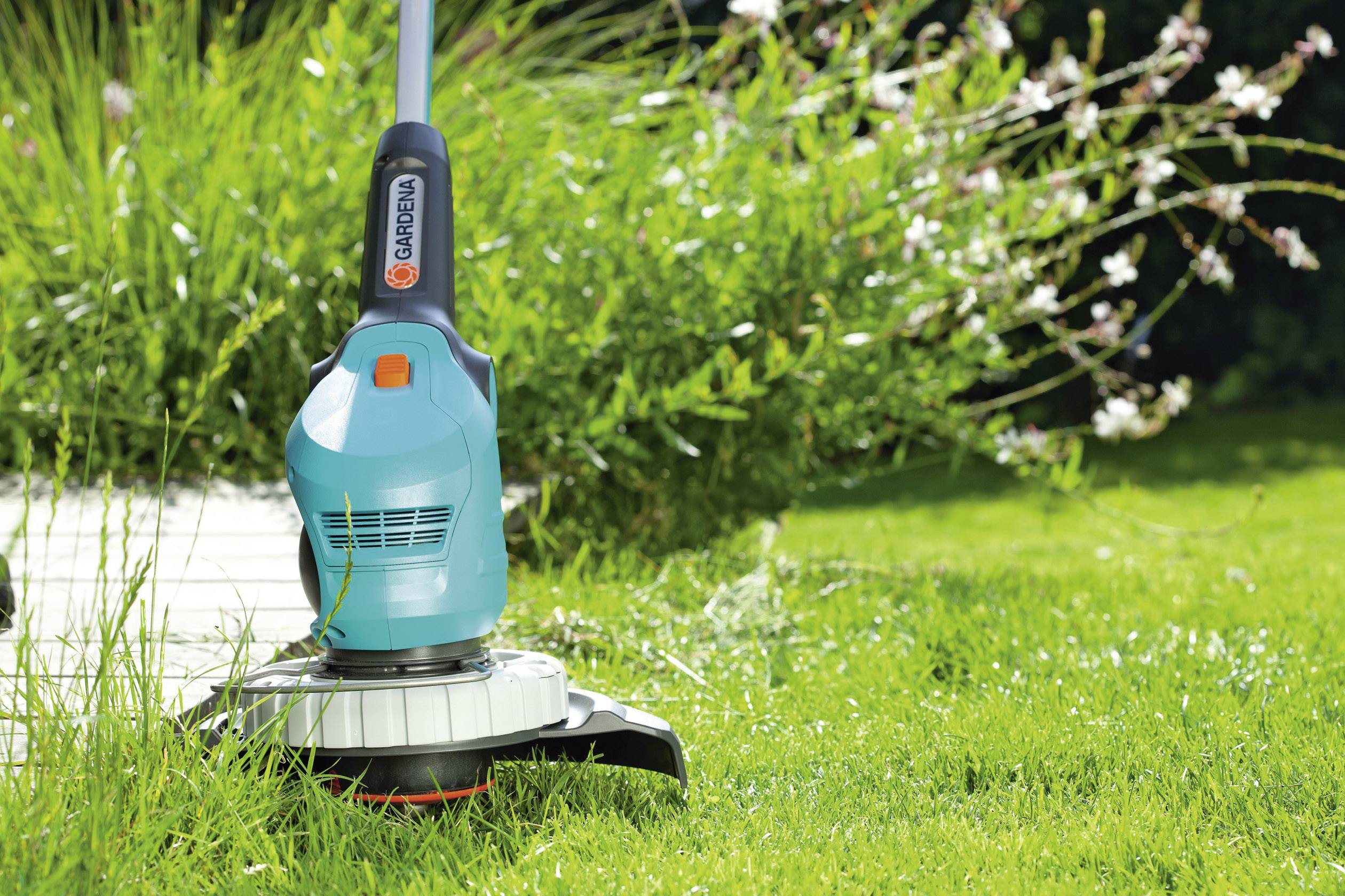 Egy személy egy kék Gardena fűszegélyvágót használ egy gondozott kert szélének lenyírásához.