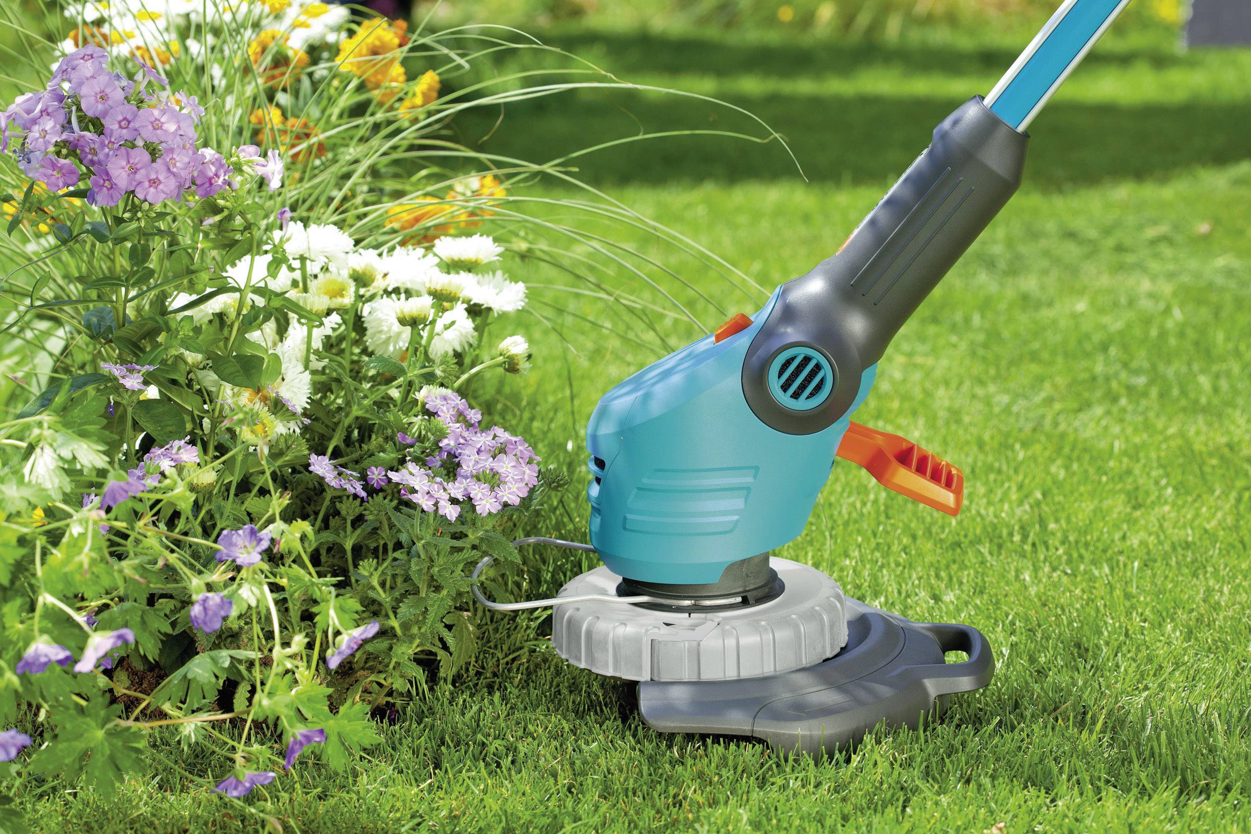 Fűnyíró vág füvet egy kertben virágzó virágok mellett. A növények közelsége kiemeli a vágás precizitását.