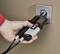 Egy kéz egy feszültségmérő műszert dugva a konnektorba, hogy lemérje az elektromos áram áramlását.