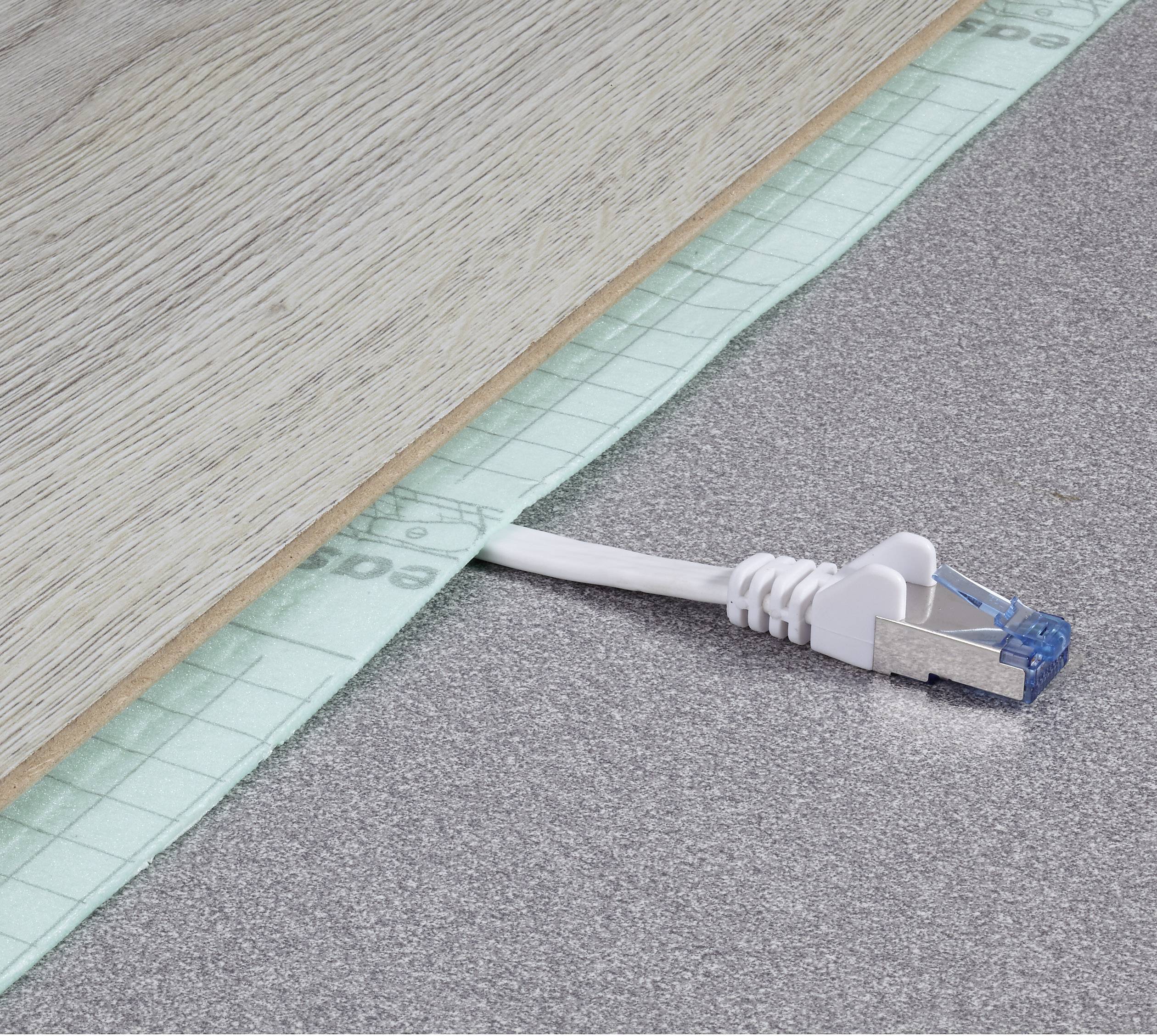 Egy Ethernet-kábel lóg ki egy falemez alól a szürke padlón. Úgy tűnik, mintha a deszkát most helyezték volna le.