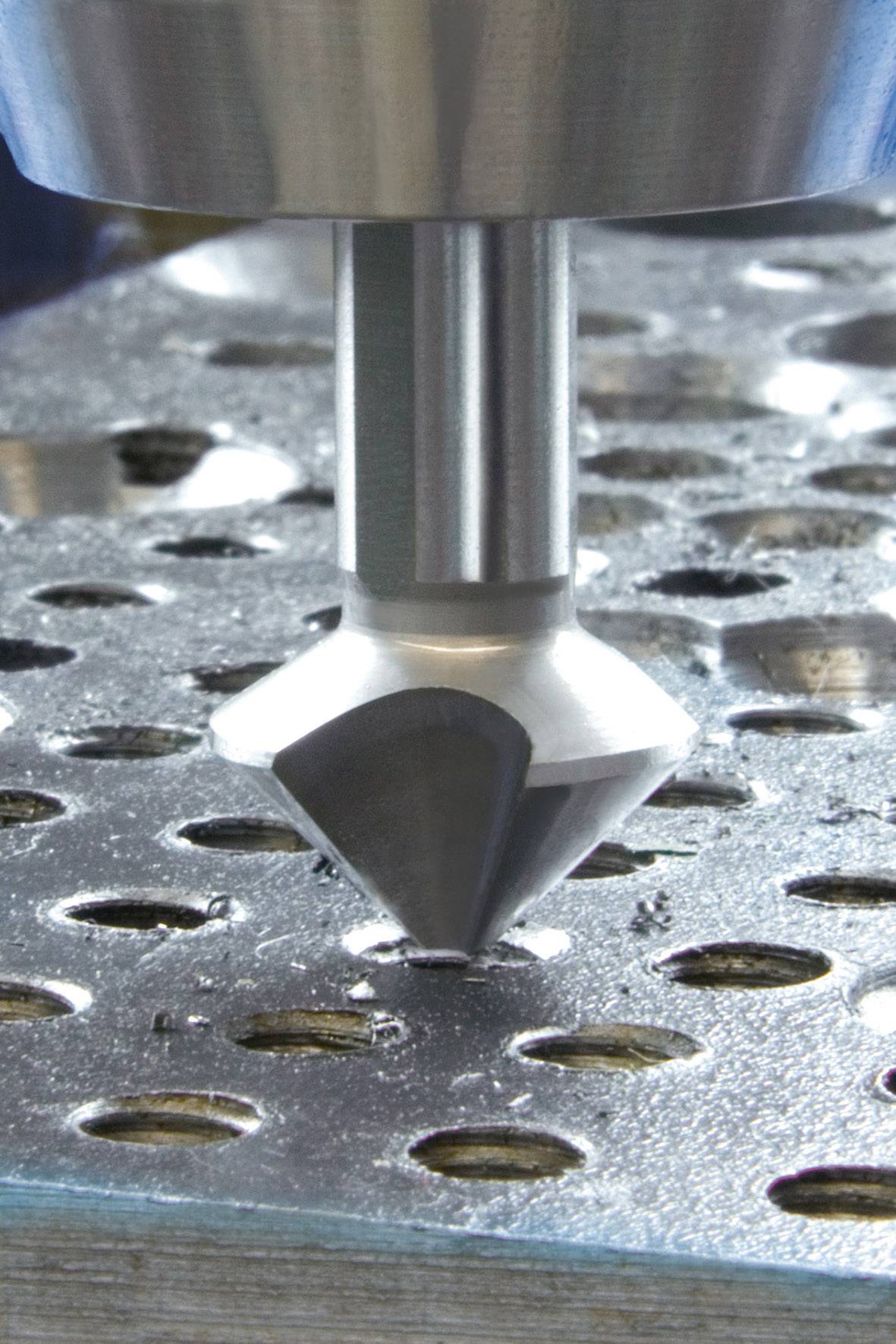 Egy fémmélyítő szerszám közeli felvétele, amint lyukakat fúr egy fémlemezbe. A szerszám kúpos fúróval rendelkezik.