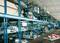 Egy nagy raktár kék fémpolcokkal, amelyek különböző autóalkatrészeket tárolnak. A polcok rendezetten vannak rendszerezve és egymásra pakolva.