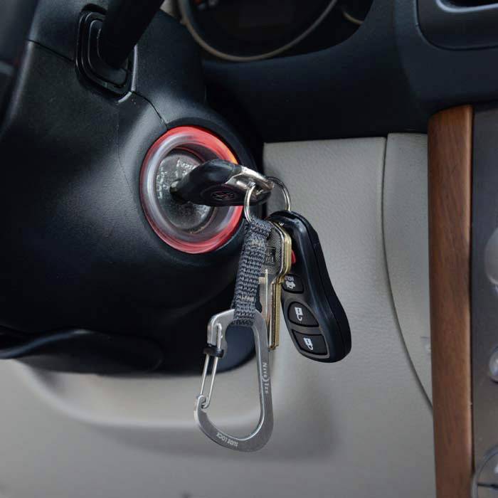 Az autókulcsok egy autó gyújtásában vannak, egy kiegészítő kulcstartóval és egy karabinerrel.