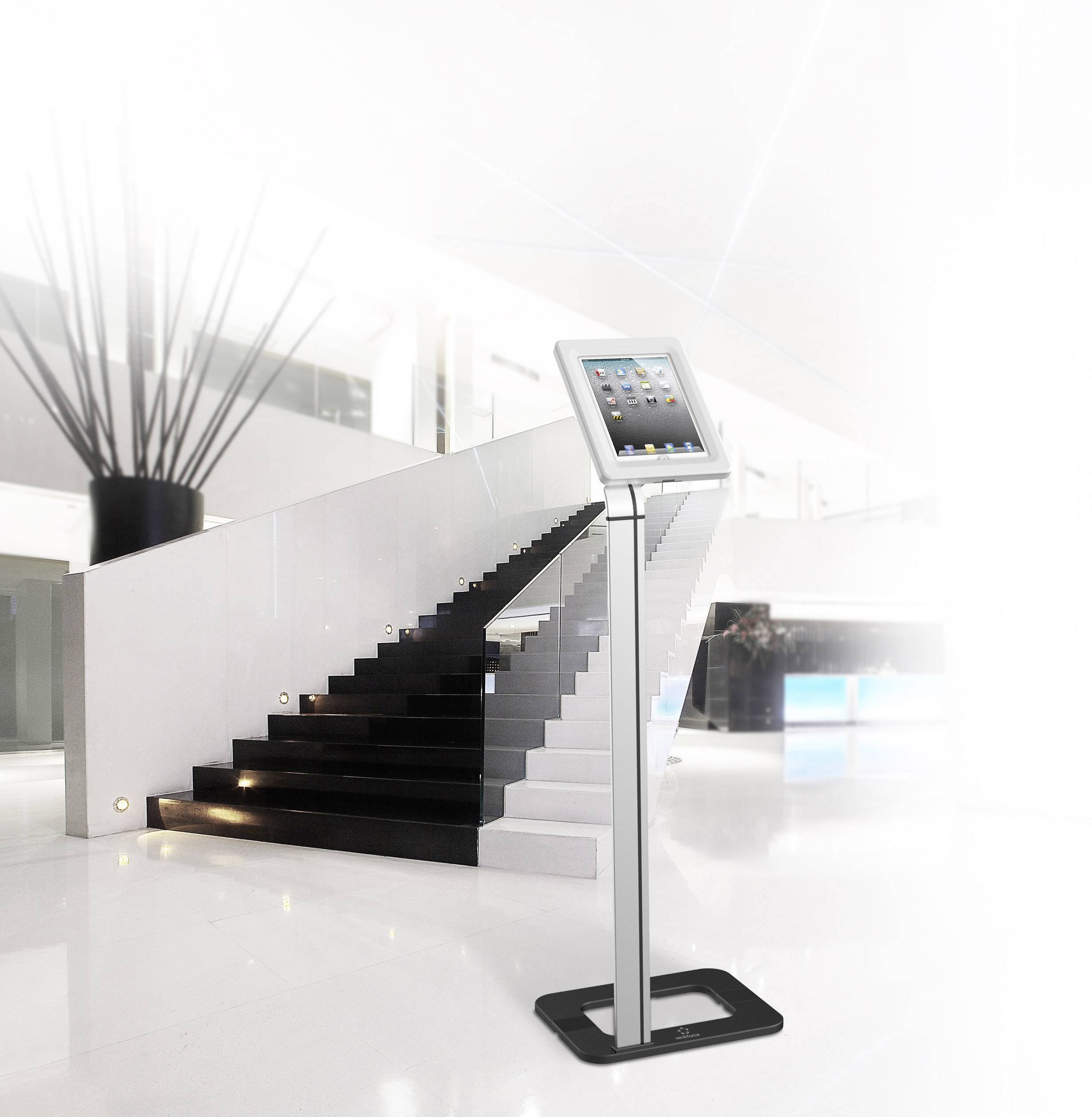 Egy tablet egy állványon áll egy modern, világos bejárati csarnokban egy lépcső előtt.