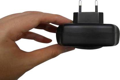 Egy kéz egy fekete töltőt tart európai típusú csatlakozóval.