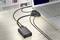 Egy laptop több kábellel csatlakozik egy HDMI-adapterhez, amely egy fa asztalon fekszik.
