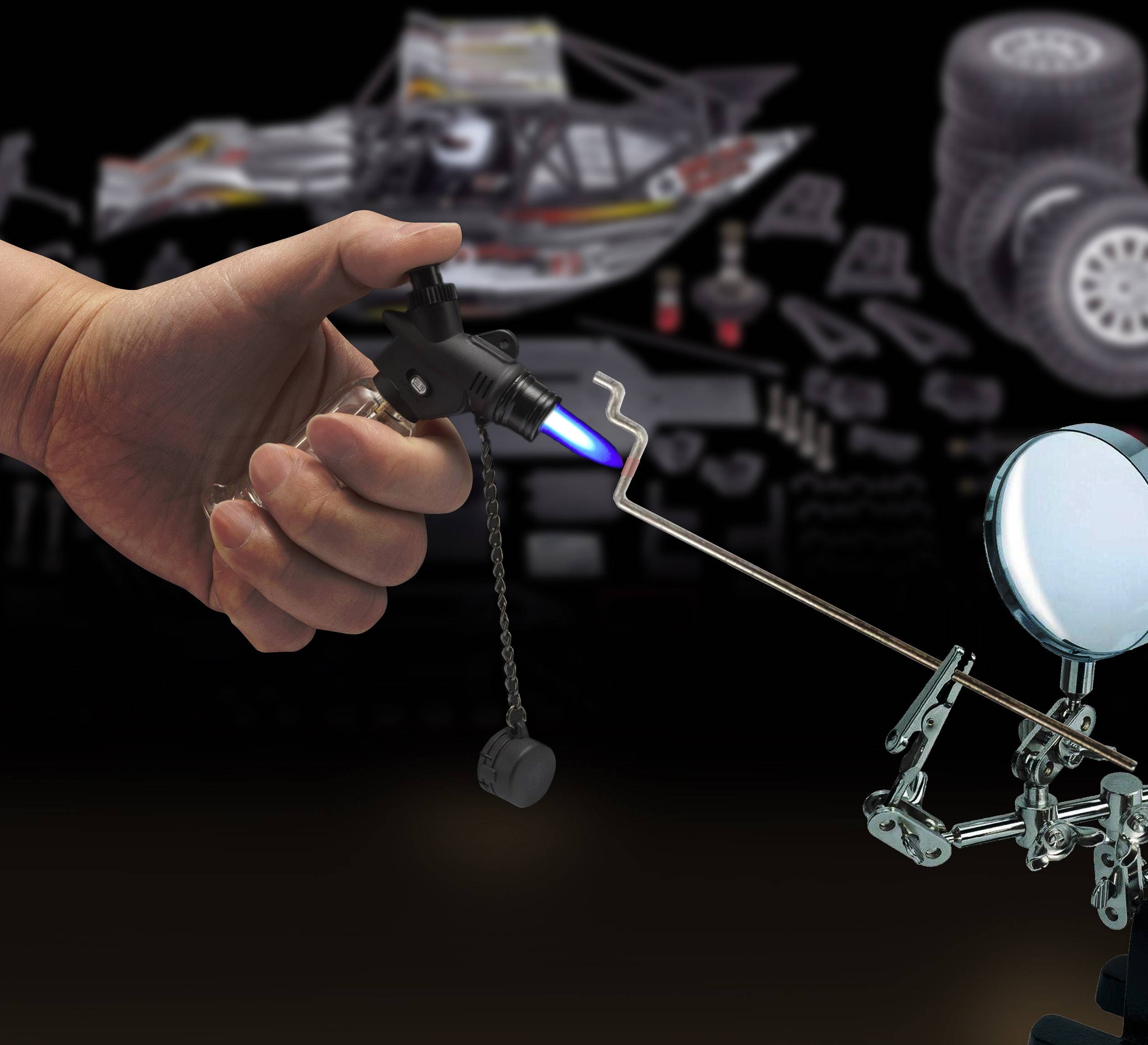 Egy kéz egy kis gázégőt tart, amely kékes lángot hoz létre. Mellette egy fémfigura áll pajzzsal és lándzsával.