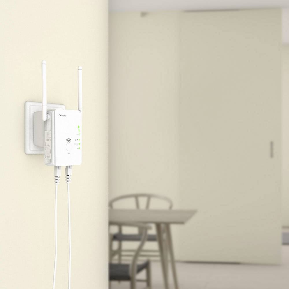 Egy WiFi-jelerősítő két antennával egy fali konnektorban van dugva. A háttérben egy asztal és székek láthatók.