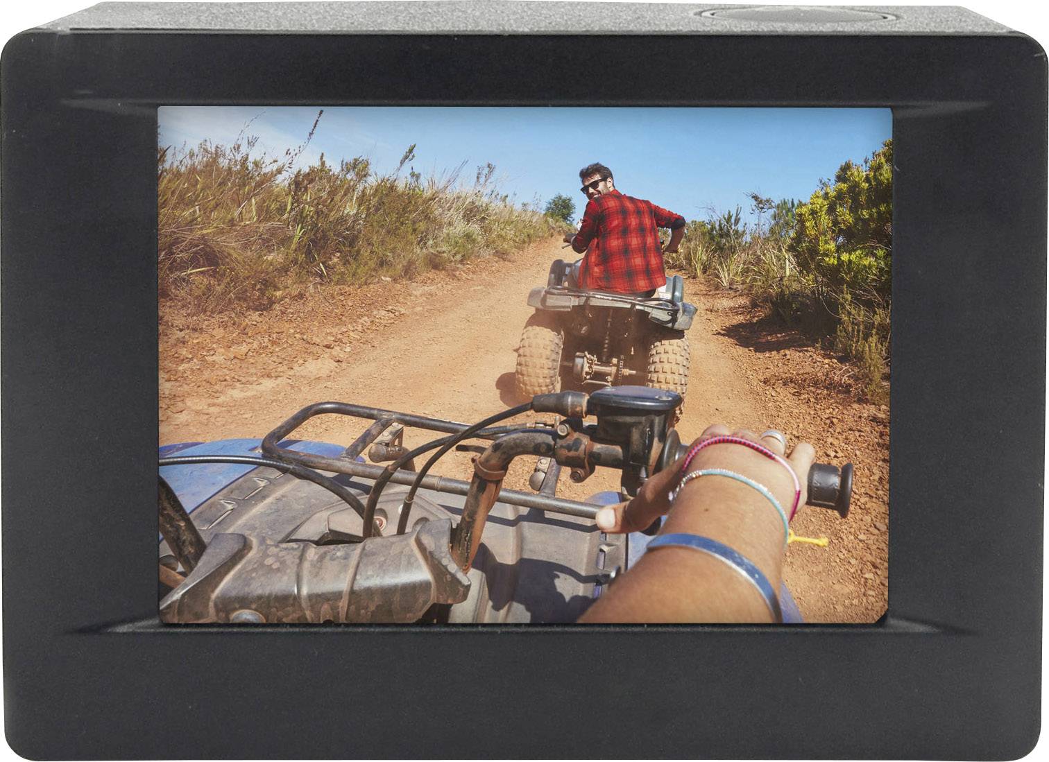 Egy piros inget viselő személy quadján halad egy poros úton egy vidéki térségben, mögötte egy másik személy.