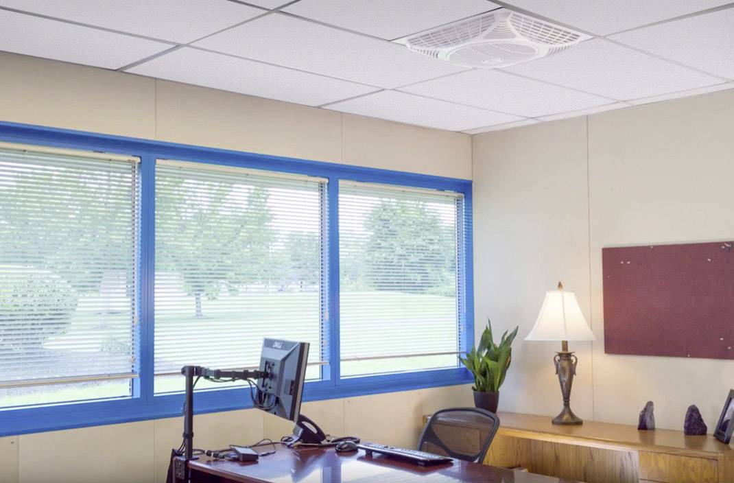 Iroda íróasztallal, székkel, számítógép-monitorral, lámpával és növénnyel. Nagy ablakok nyújtanak kilátást kifelé, fákkal és füves területtel.