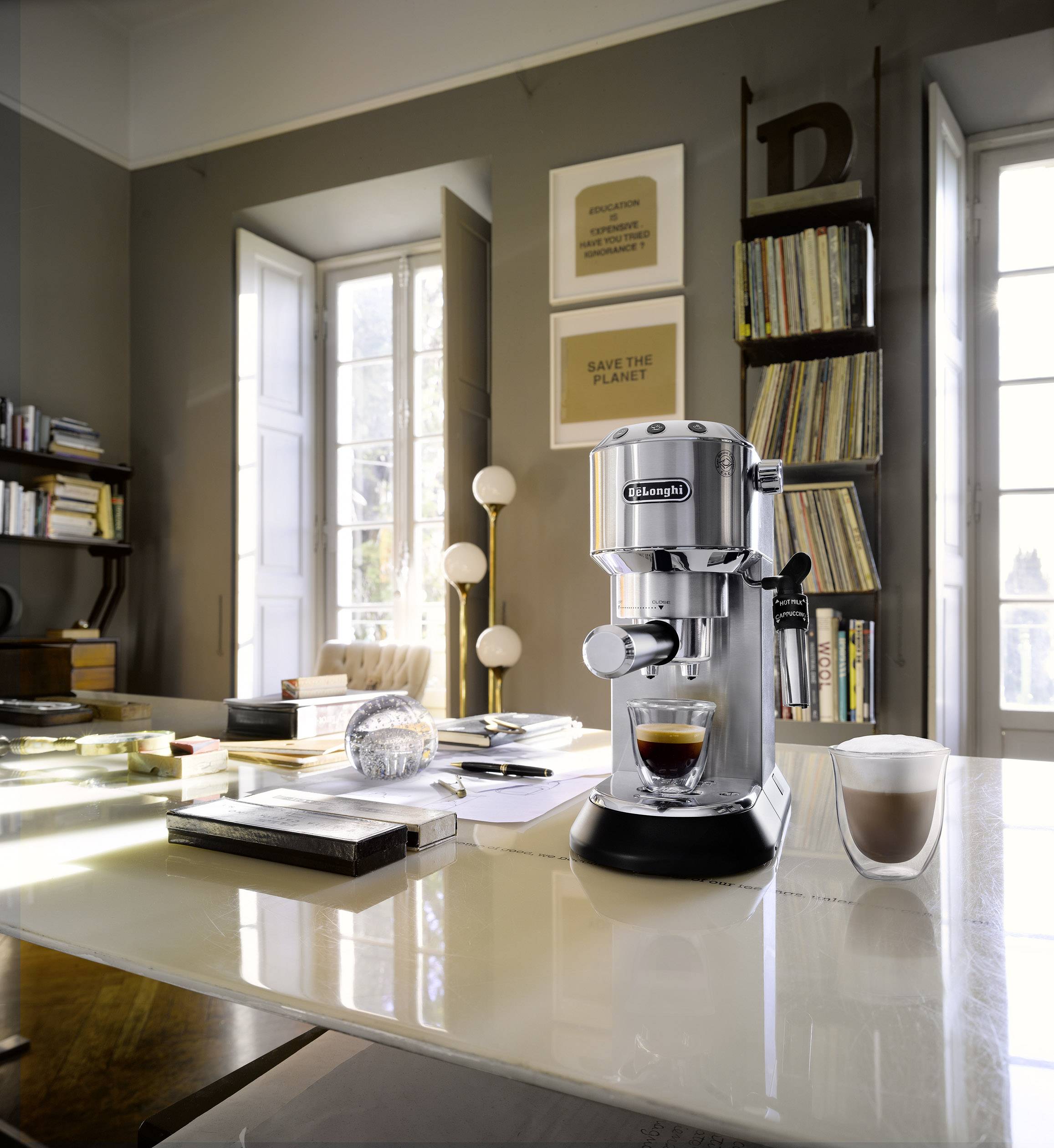 Kávégép egy asztalon egy jól megvilágított helyiségben, egy eszpresszóval és egy cappuccinóval. A háttérben polcok és egy ablak.
