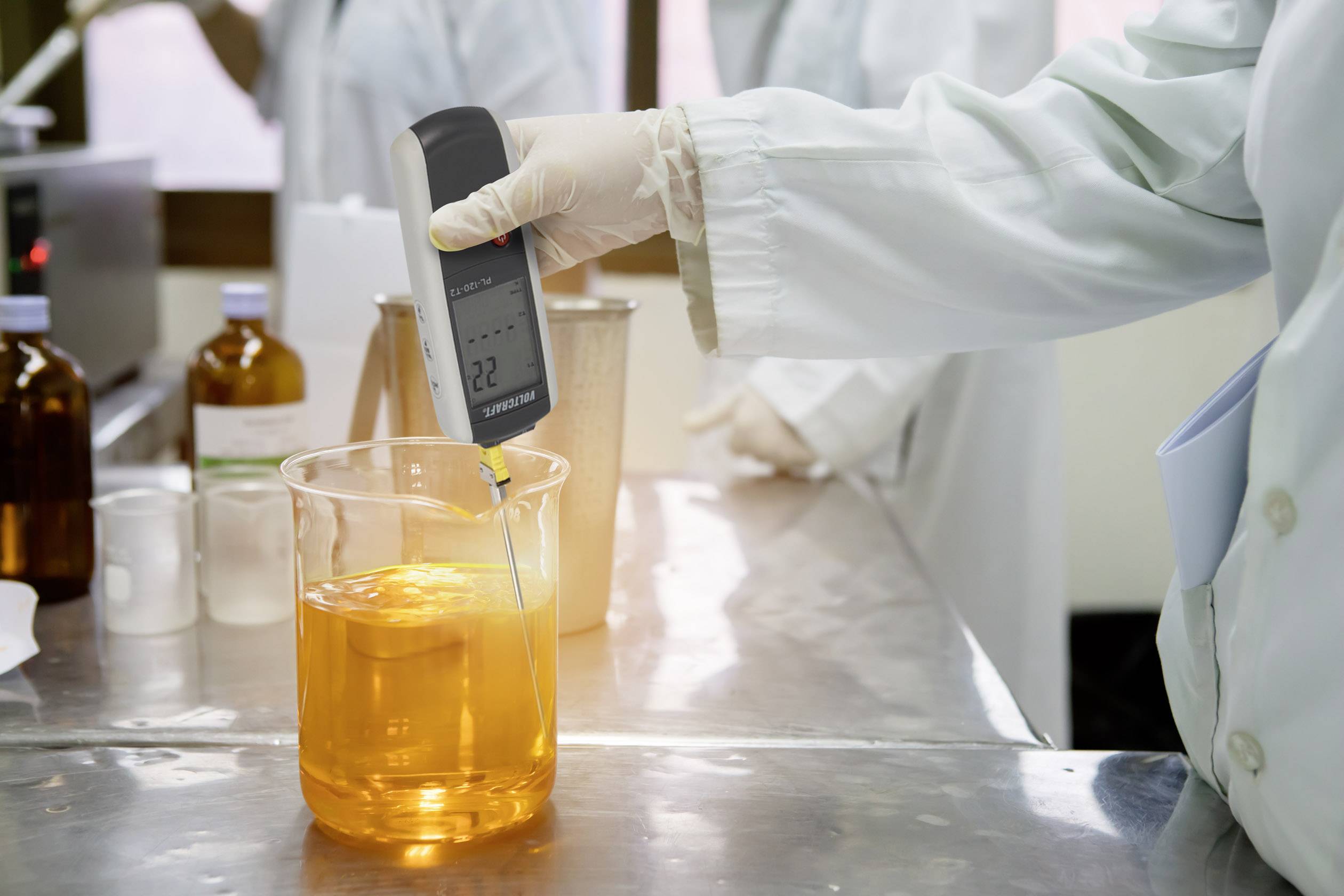 Egy laboratóriumi dolgozó kézi pH-mérővel méri egy narancssárga folyadék pH-értékét egy főzőpohárban.