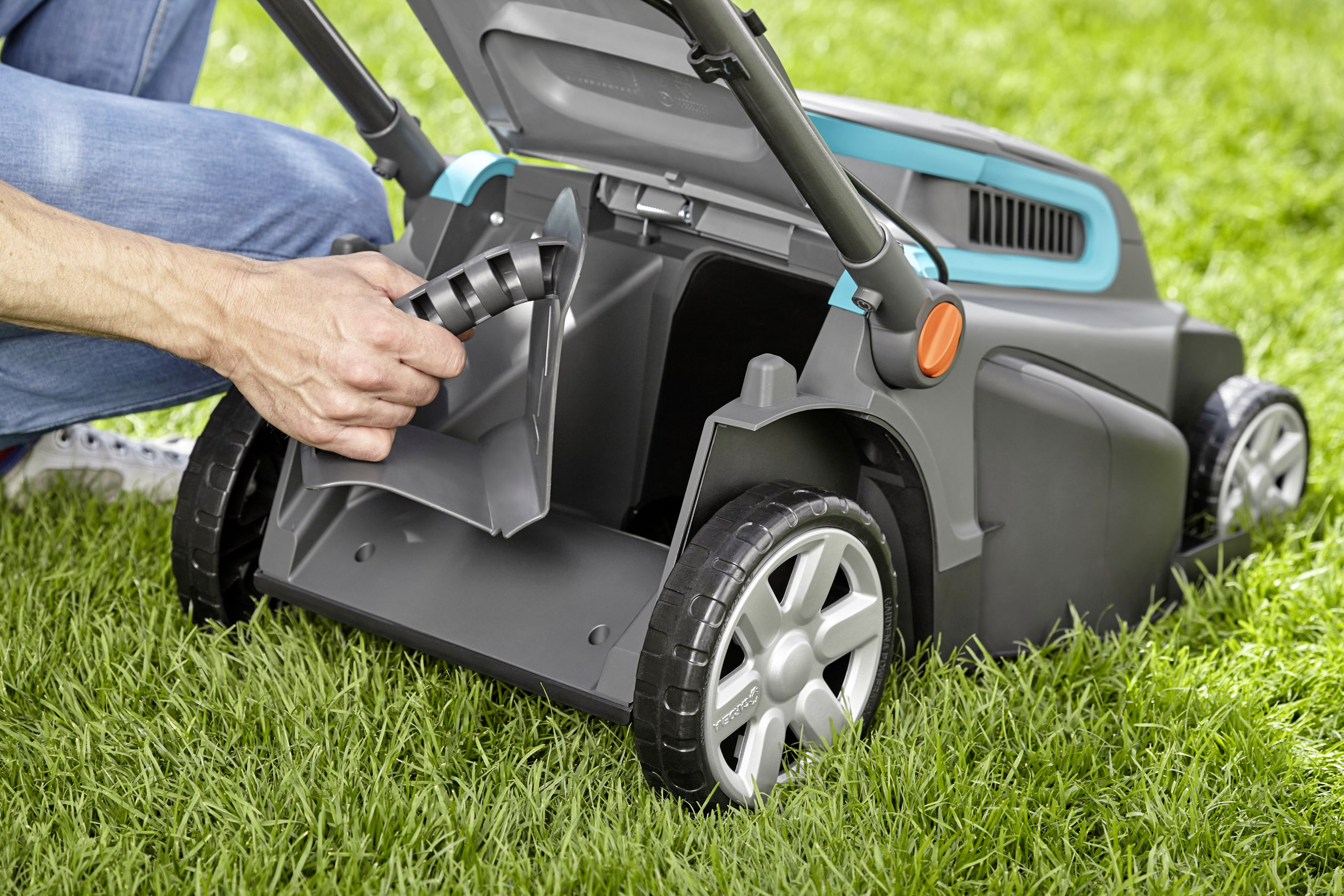 Egy személy elemet helyez be egy fűnyíróba. A fűnyíró zöld füvön áll, és nyitott akkumulátortartó fedéllel rendelkezik.