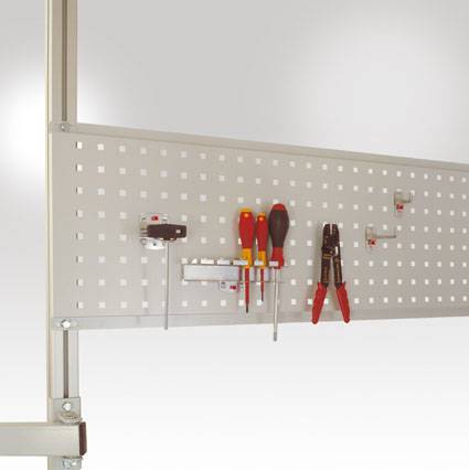 Fémtartó sín négyzetes lyukakkal egy fal mentén, különböző szerszámokkal rendszerezve, mint például csavarhúzók és fogók.