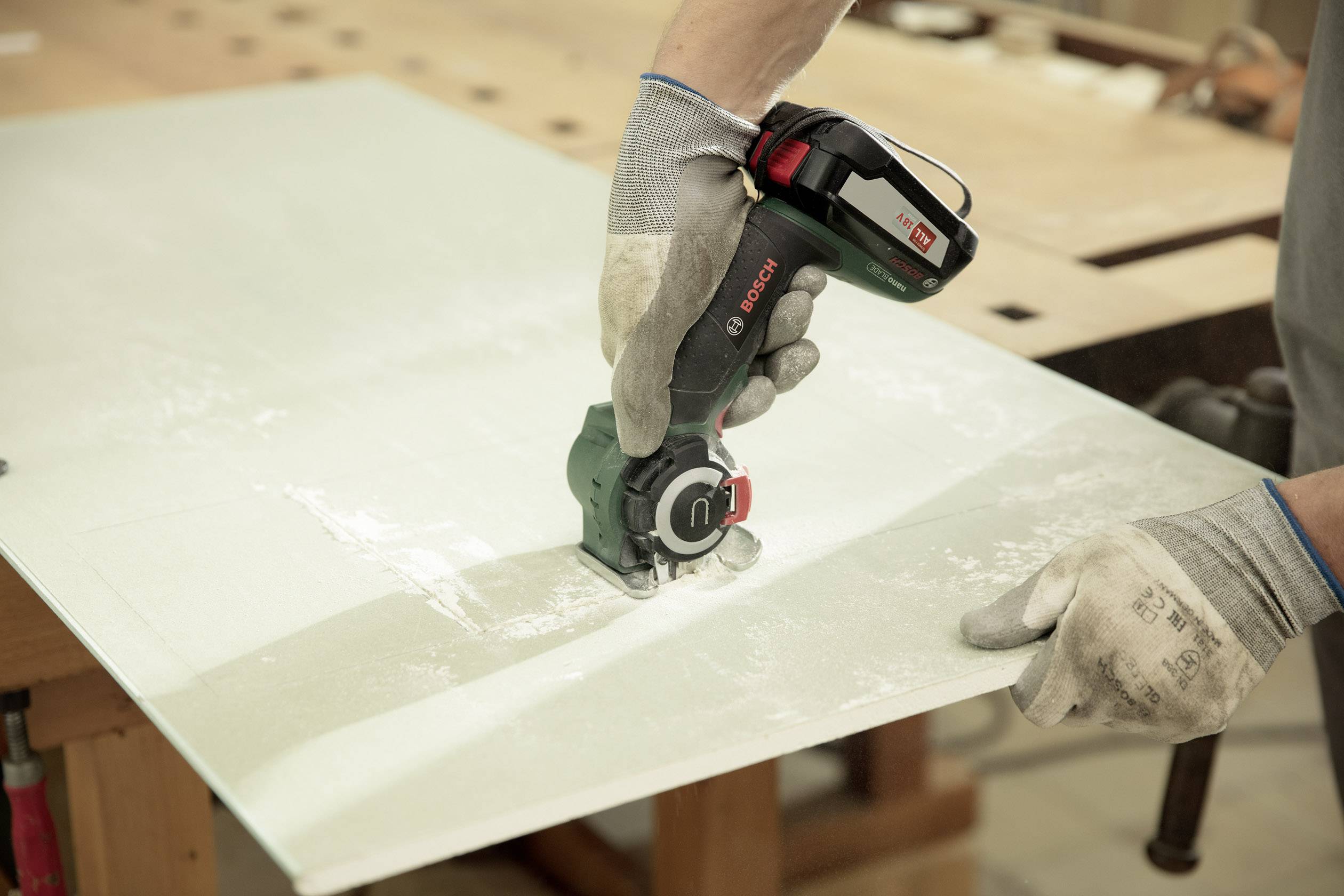 Egy személy egy Bosch vágógéppel üvegeket vág egy asztalon. A személy védőkesztyűt visel.