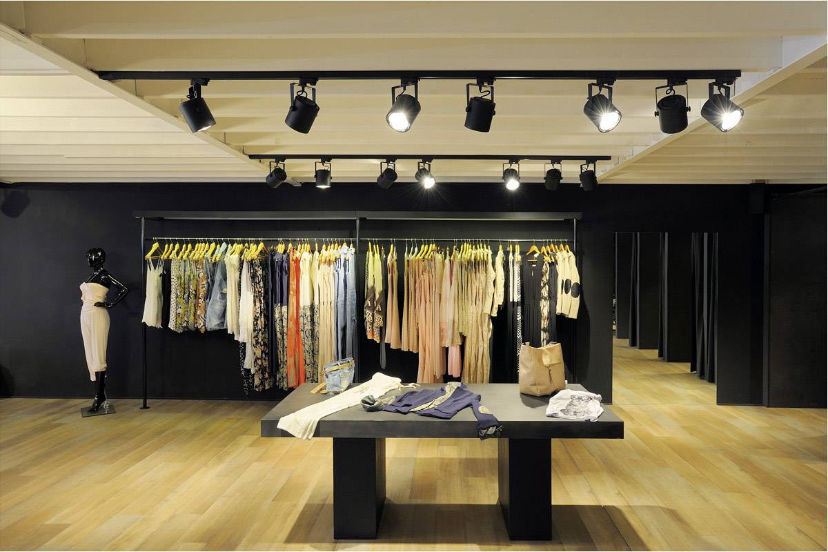 Egy modern divatüzlet tere fa padlóval, ruhafogasokon színes ruhákkal, középen egy asztallal, amelyen összehajtogatott ruhadarabok fekszenek.