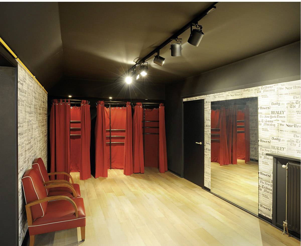 Öltöző piros függönyökkel, tükörrel és piros székekkel. A mennyezeti spotlámpák megvilágítják a helyiséget.