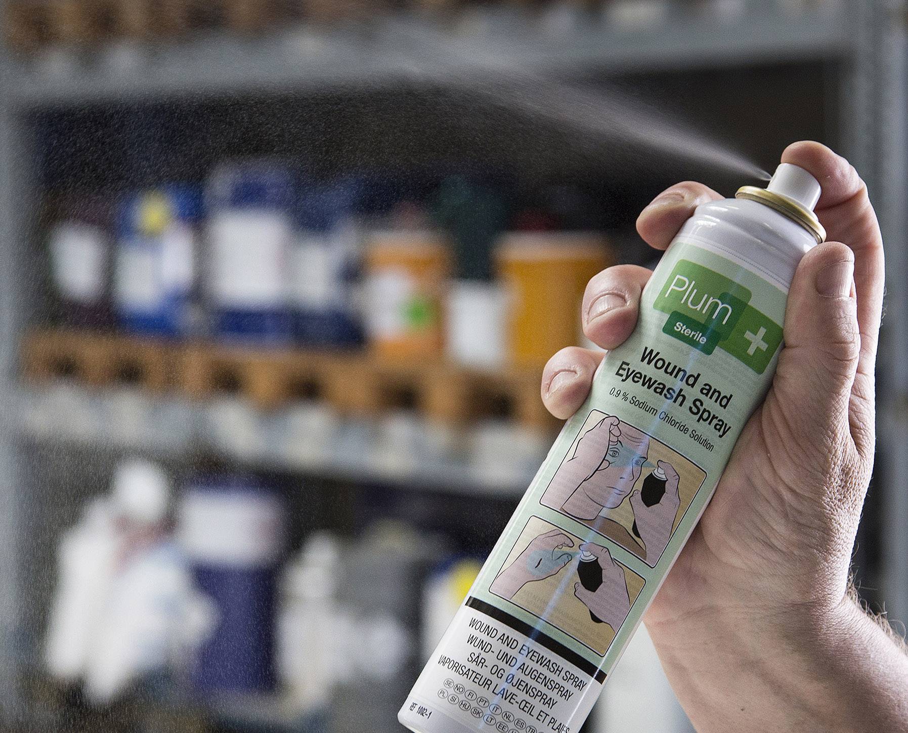 Egy kéz egy spray-t tart, amelynek felirata 'Szilva Sebkezelő és Szemöblítő Spray'. A háttérben elmosódott polcok láthatók.