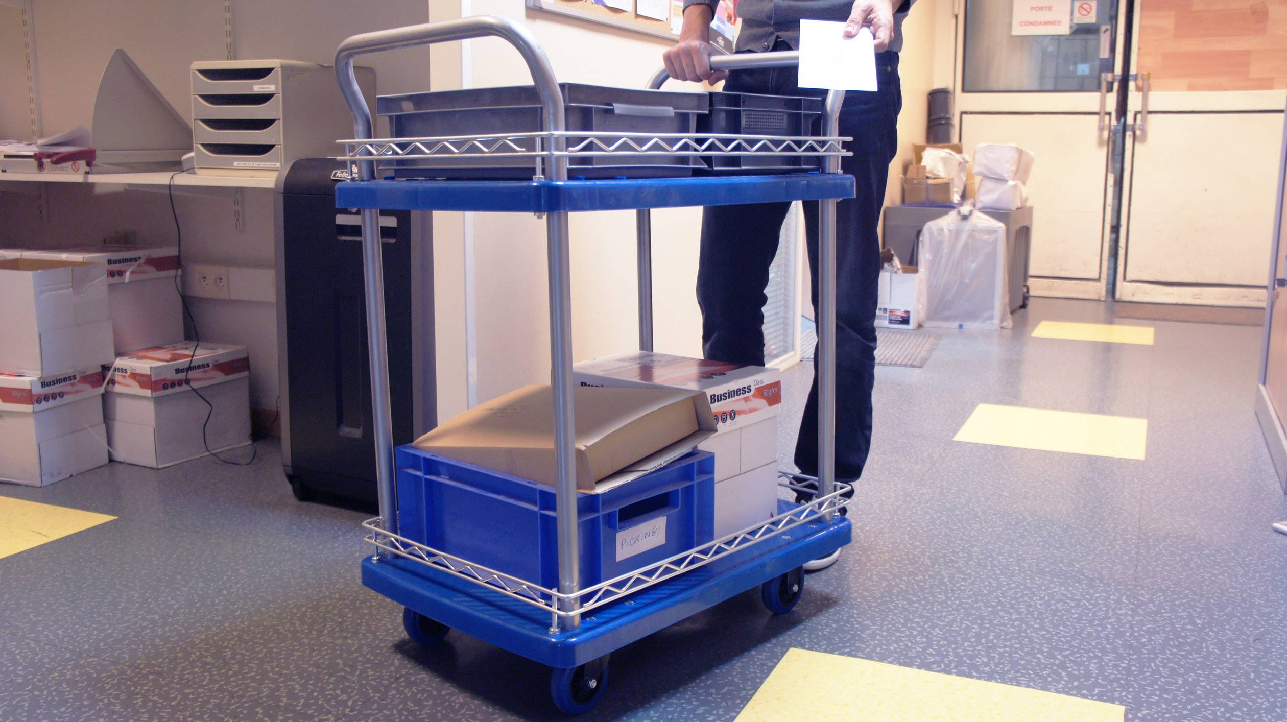 'Egy személy egy ládát szállít egy gurulós kocsin egy irodafolyosón.'