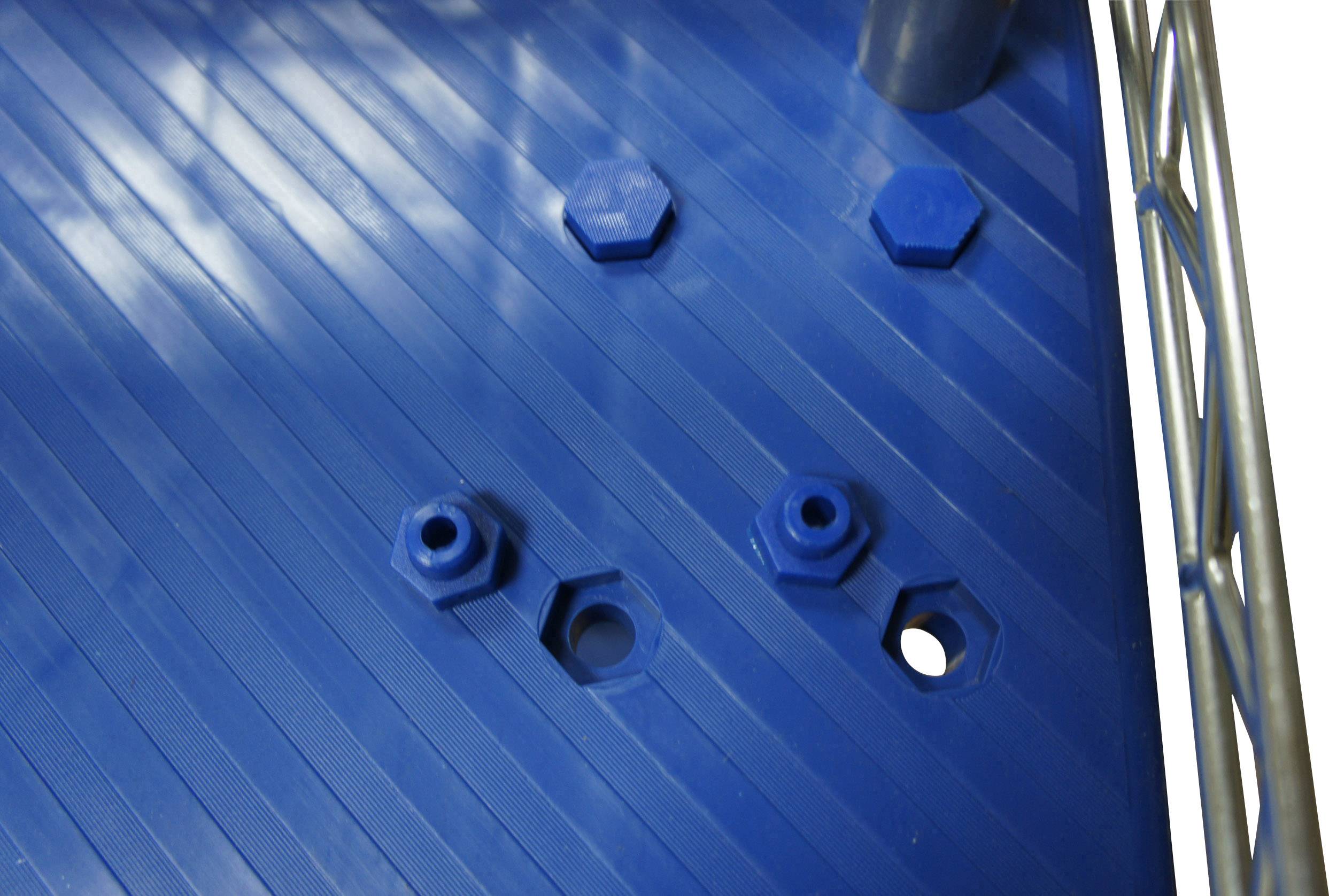 Hatszögletű anyák és csavarok kék, bordázott padlóburkolaton, részben kivágásokba süllyesztve. Fémkeret látható mellettük jobbra.