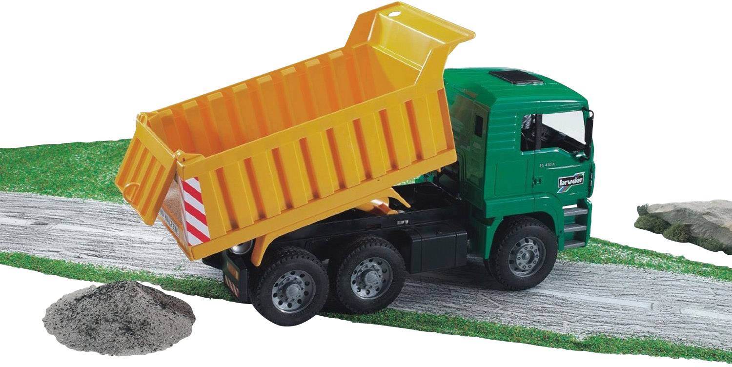 Egy zöld teherautó narancssárga billenőplatóval épül törmeléket rak le egy építkezésen. Balra egy homokdomb fekszik.