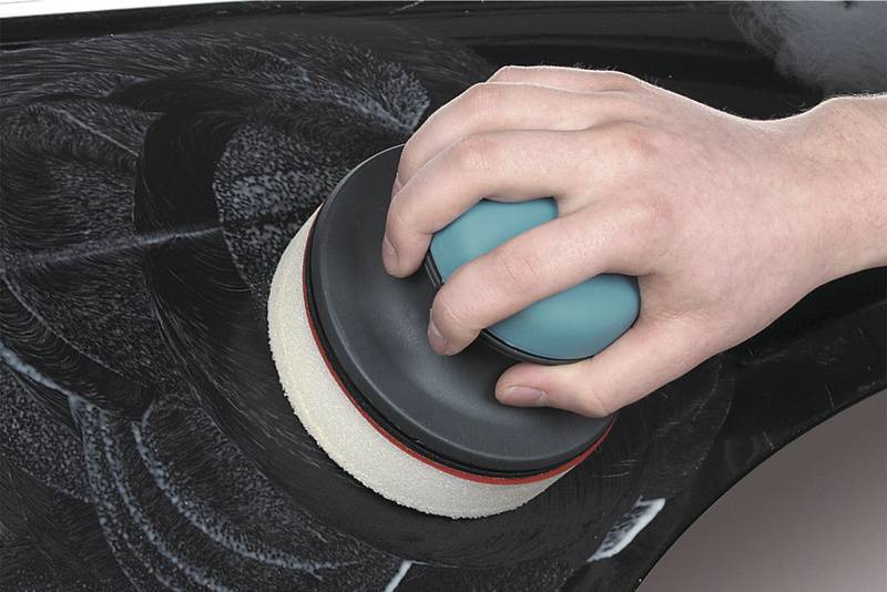 Egy kézi eszközt egy polírozófeltéttel egy személy használ egy fekete autólakkfelület polírozásához.