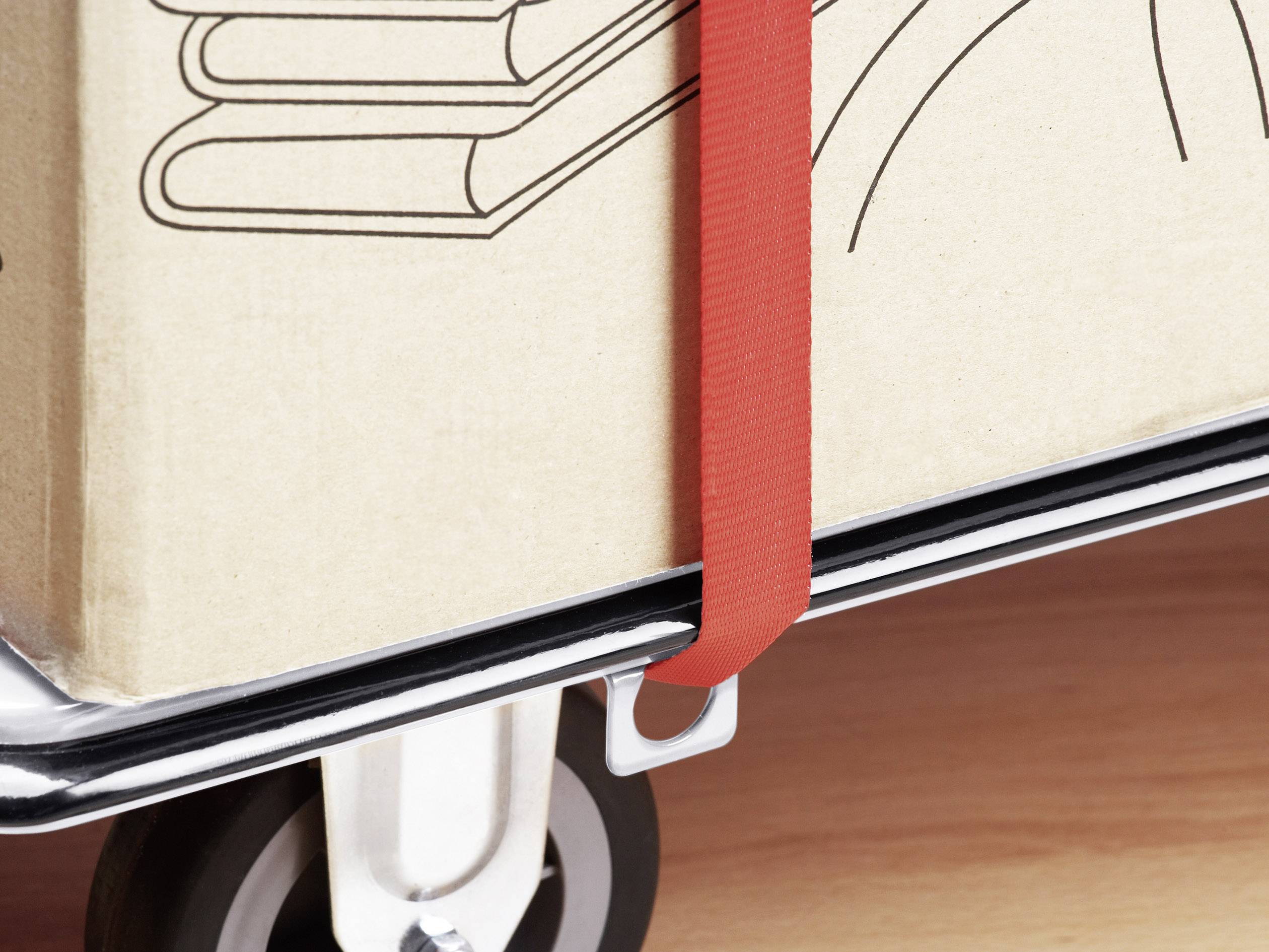 Egy doboz könyvszimbólumokkal egy piros szíjjal rögzítve van egy szállítókocsira. A padló fából készült.