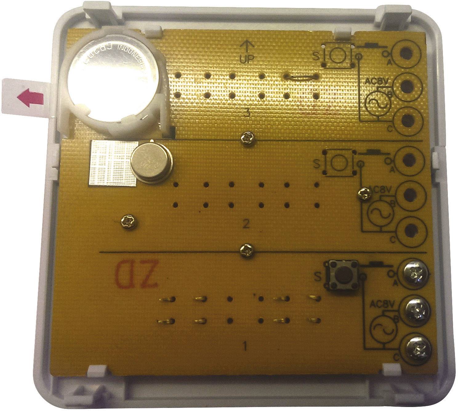 Egy elektronikus eszköz több áramköri lappal és gombbal. Egy kisméretű akkumulátor található a felső bal sarokban.