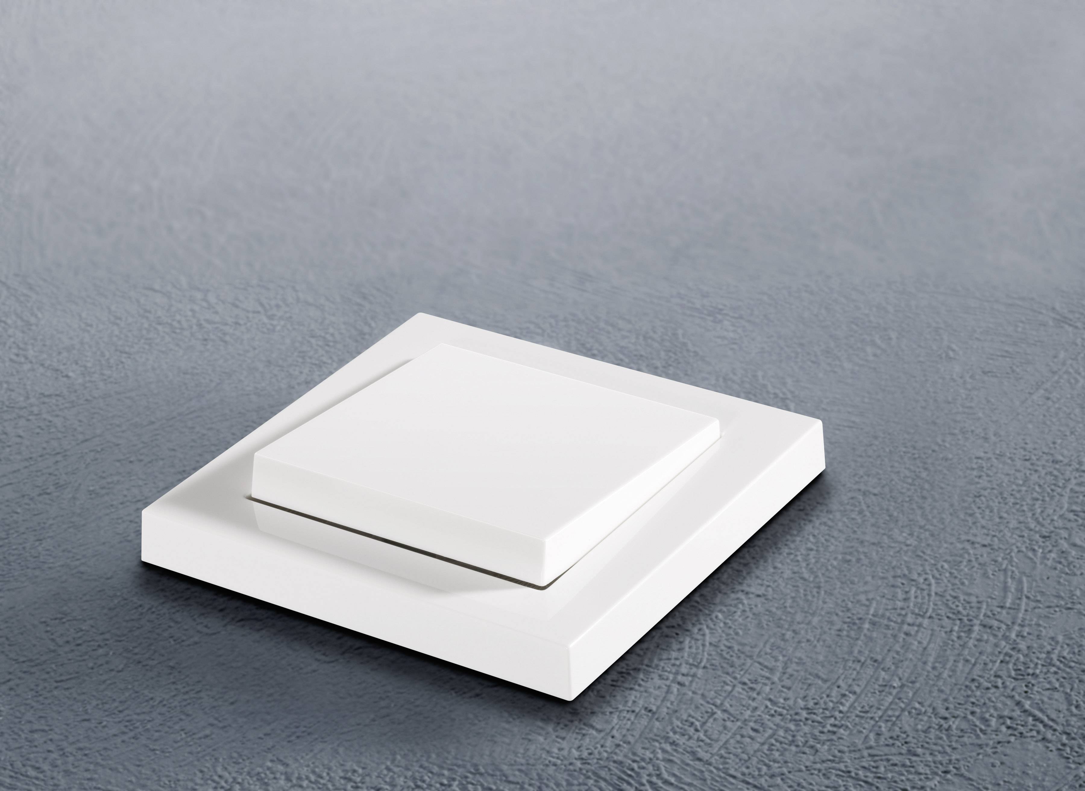 Egy modern, négyzet alakú, fehér villanykapcsoló egy szürke falon.