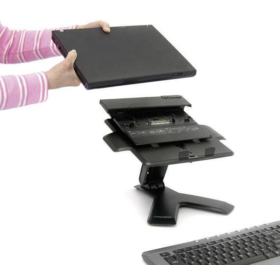 Egy személy egy laptopot emel le egy dokkolóállomásról, amely egy billentyűzet mellett egy íróasztalon helyezkedik el.