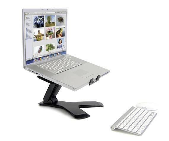 Egy laptop áll egy fekete állványon, amelynek képernyőjén képek láthatók. Előtte egy külső billentyűzet és egér fekszik.