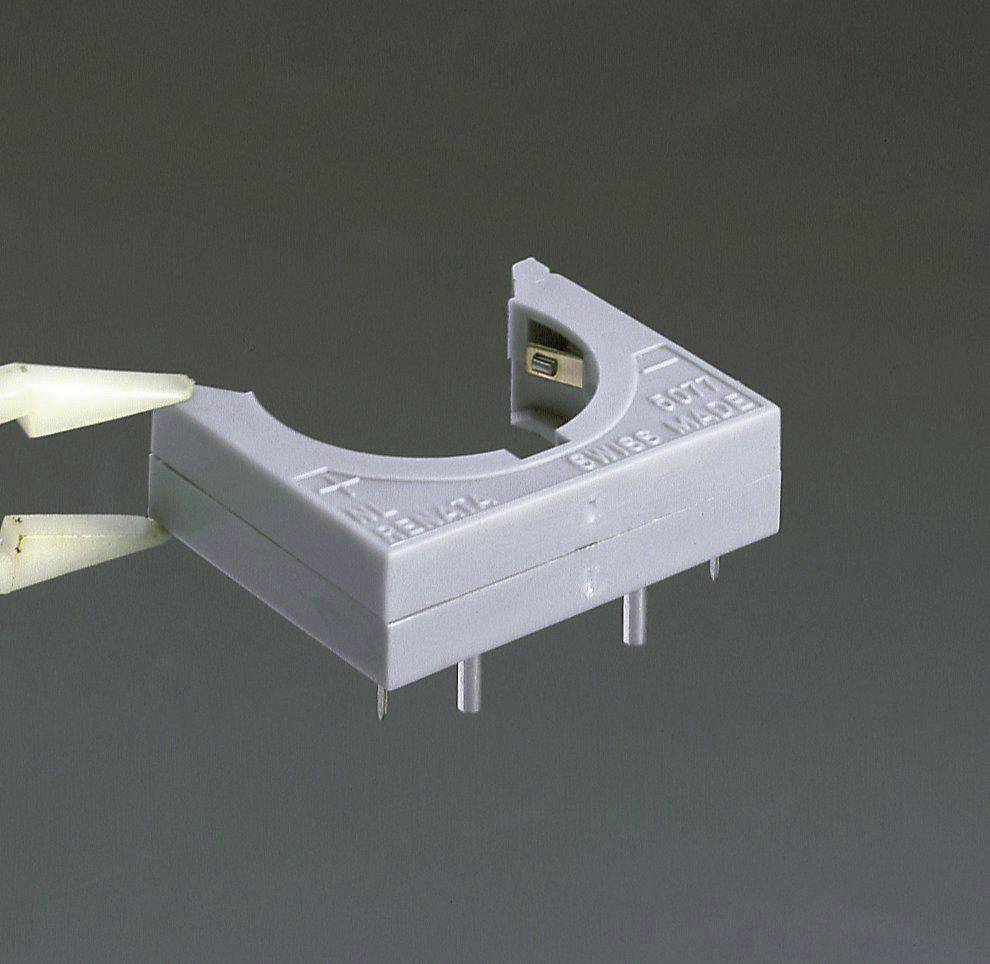 Egy szürke alkatrész, amelynek íves formája van és két látható csatlakozója van, egy fehér robotkar tartja.