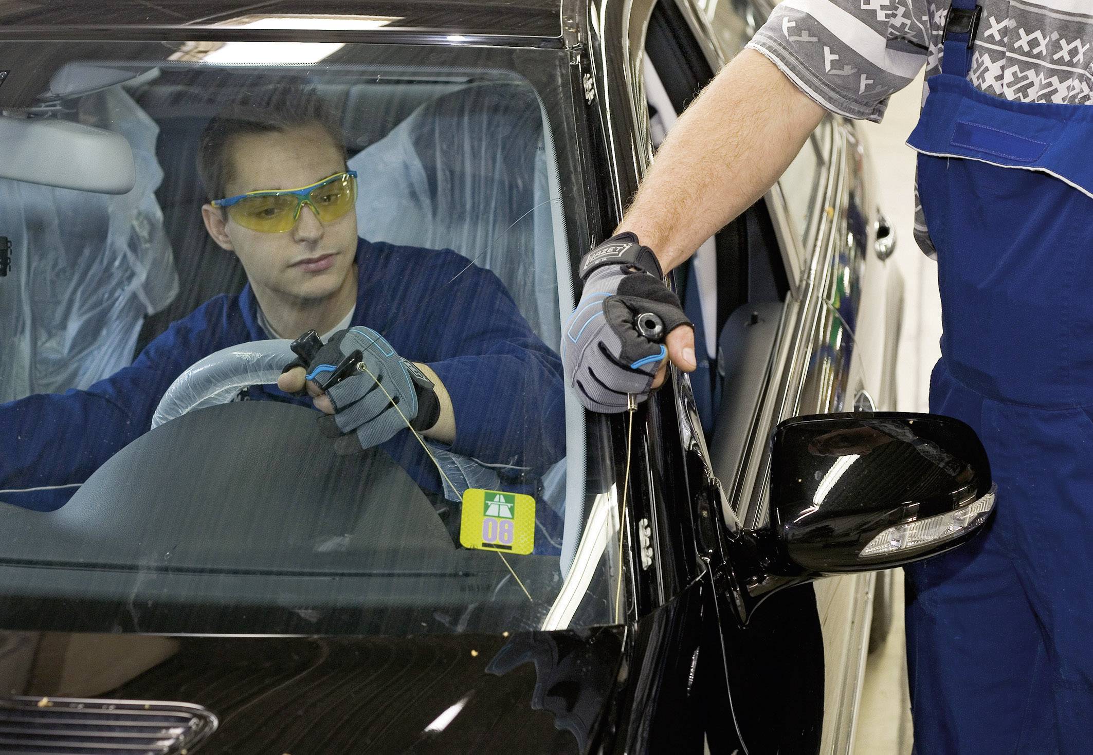 Egy személy az autóban a fűthető ablakot ellenőrzi, miközben egy szerelő kívülről megvizsgálja az ablakemelőt.