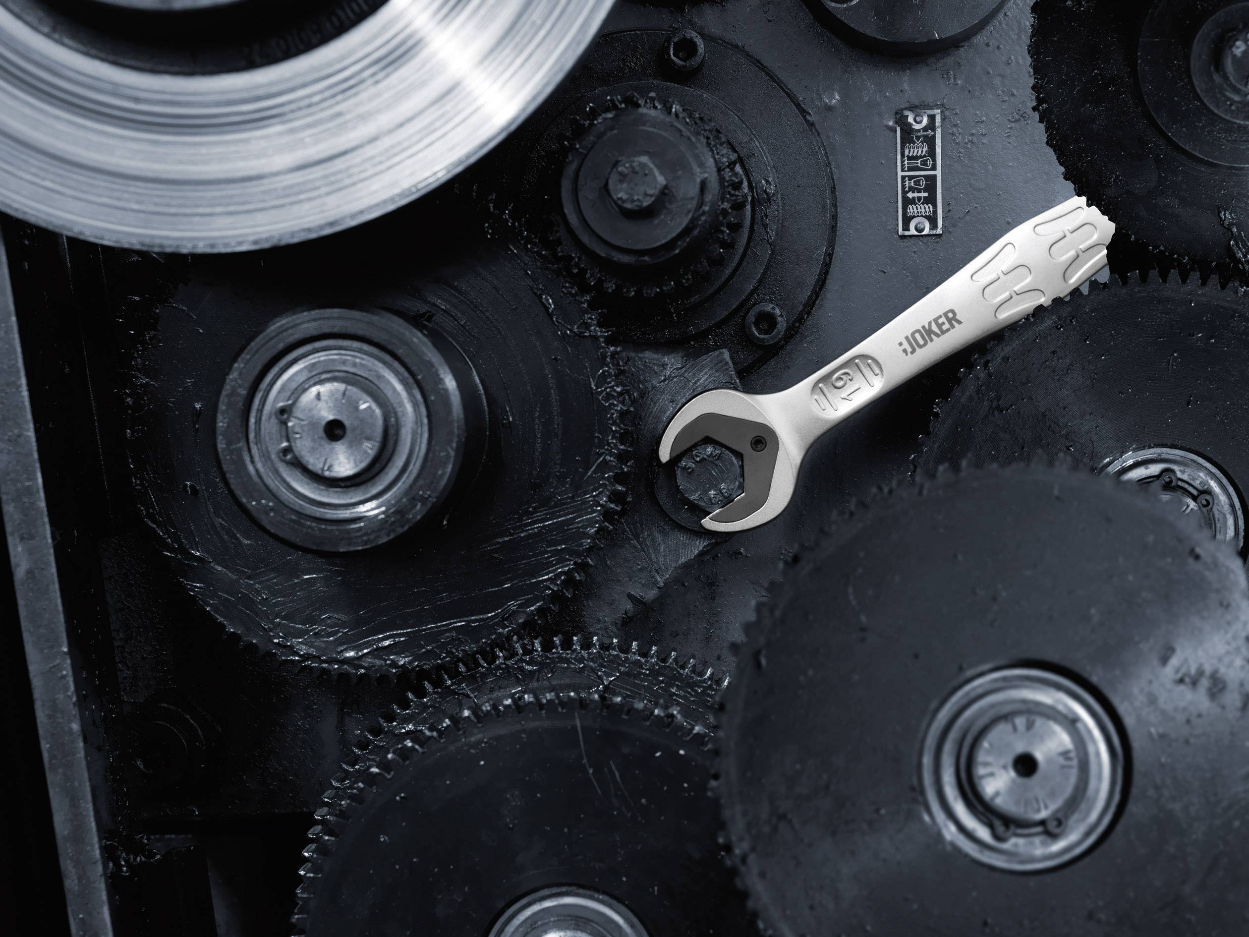 Egy ezüstös csavarkulcs fekszik egy nagy fogaskeréken egy több egymásba kapcsolódó fogaskerékből álló mechanizmusban.